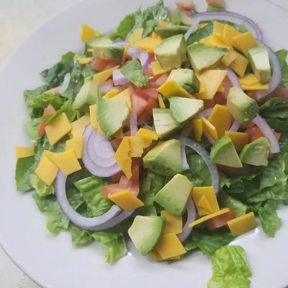 A fresh diner salad with green lettuce, avocado, red onion, tomato, and cheddar cheese.