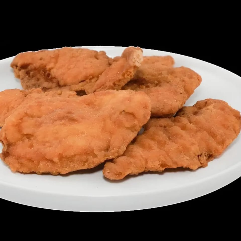 A white plate holds several golden-brown, breaded chicken cutlets, ready to be served.