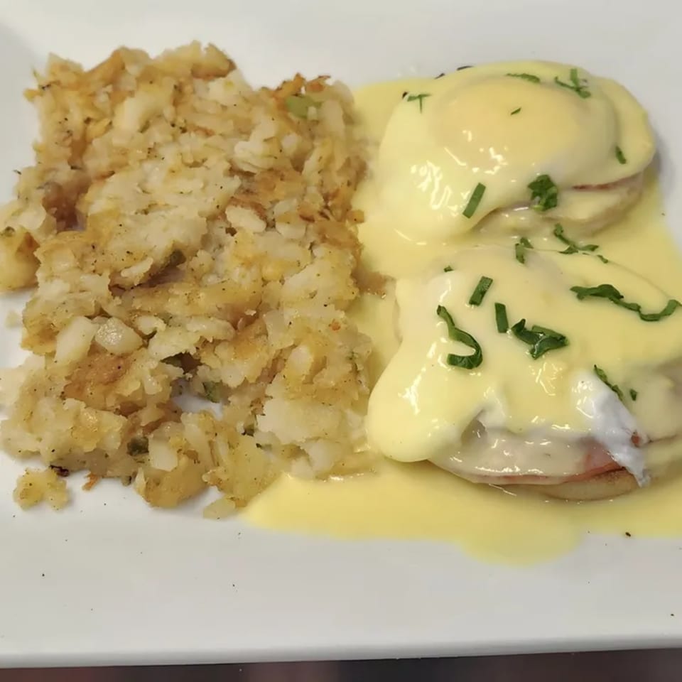 Eggs Benedict with hollandaise sauce and chives, served with a side of crispy hash browns.